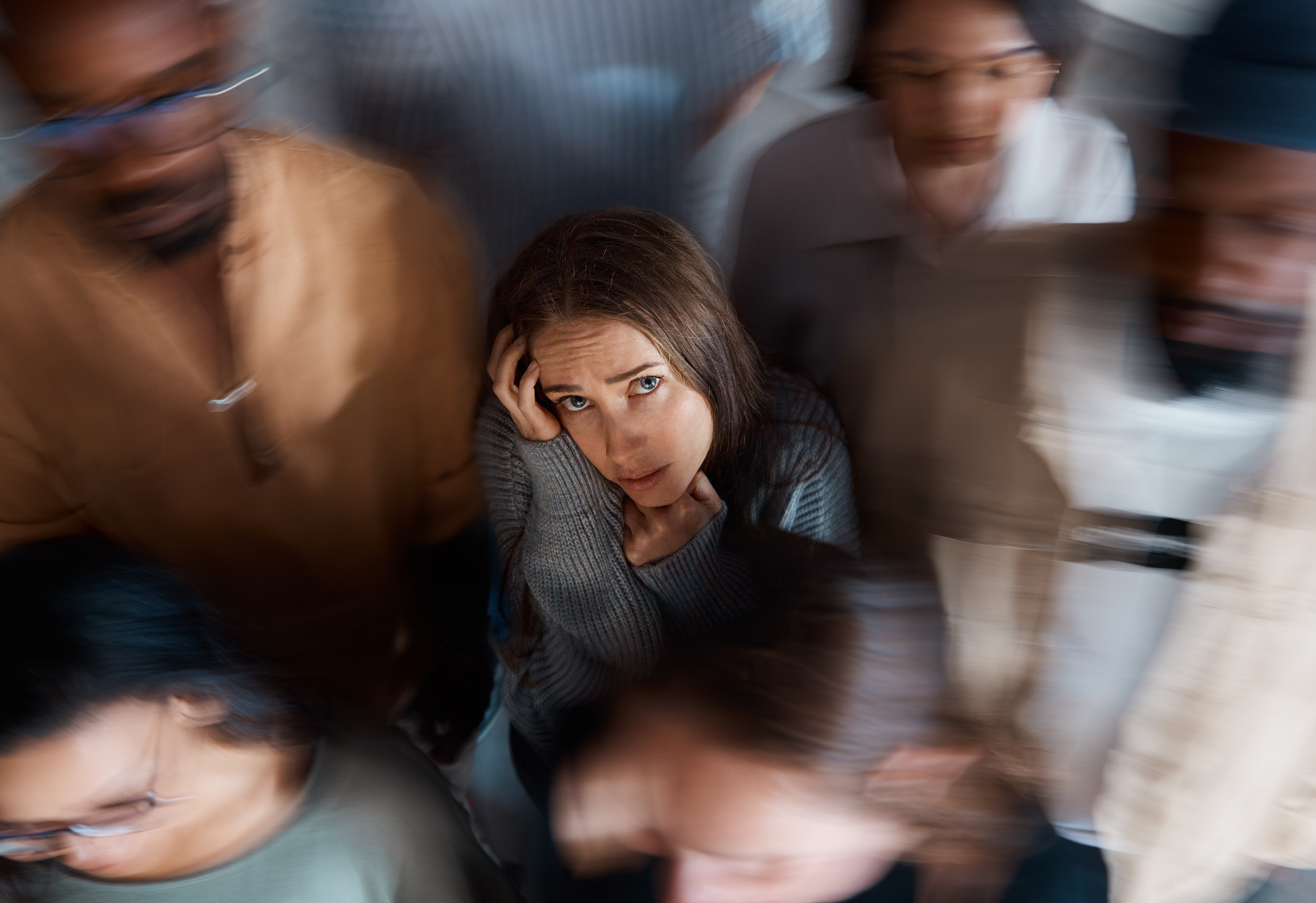 Alone in a room full of people. Shot of a young woman sitting on the floor with people around her